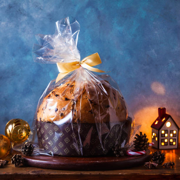 włoski świąteczny chleb panetton z przezroczystym opakowaniem na stole ozdobionym na boże narodzenie. i dwie szklanki szampana. noworoczny tradycyjny deser - fruitcake christmas cake cake raisin zdjęcia i obrazy z banku zdjęć