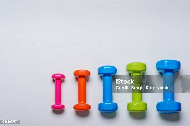 Many Blue Green And One Orange In The Middle Dumbbells On A White Background Concept Preparing To Fitness Sports Equipment Top View Mock Up Stock Photo - Download Image Now