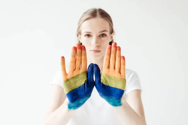 Young woman showing stop hand-sign with painted rainbow isolated on white