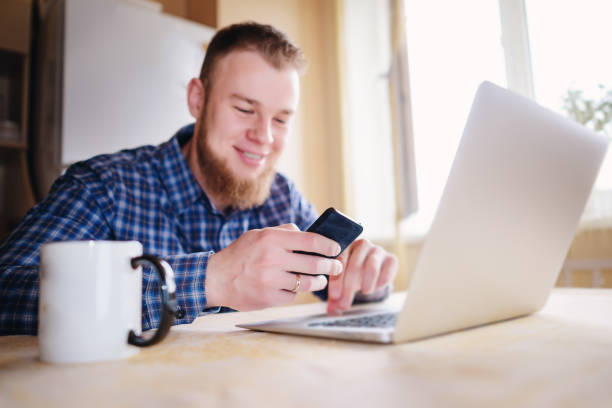 istock Man using laptop and smart phone at the table in office against the window 916164352