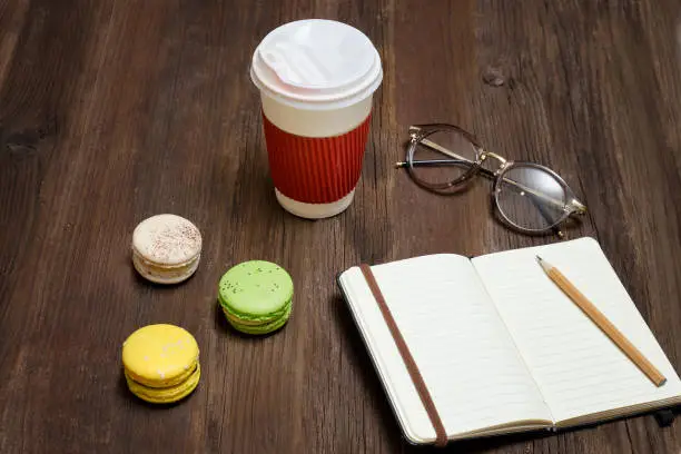 Open notebook with a pencil. Macaroons, paper-cup and a credit card. Wooden background. Top view