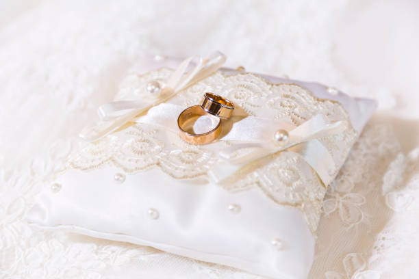 istock Two gold shiny wedding rings together on satin lace pillow 916183476