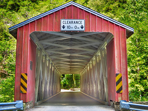 Historic red Frazier Lairdsville wooden covered bridge located in Lycoming County Pennsylvania.  Built over Little Muncy creek in 1888 and placed on the National Register of Historic Places. Photographed against blue cloud sky with Little Muncy Creek flowing under the bridge.  Still able to drive through the bridge as of this date.