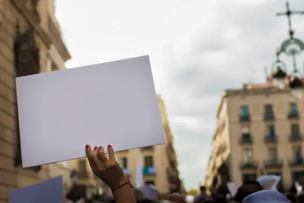 woman's hands in the foreground holding a blank banner to put the message you want during a demonstration in the streets of an European city
