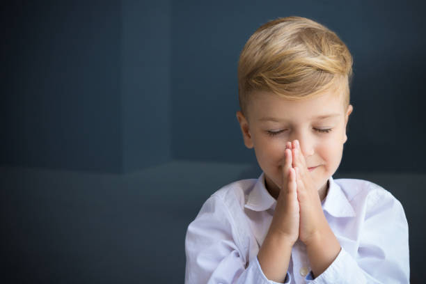 Little boy in namaste position meditating with eyes closed.