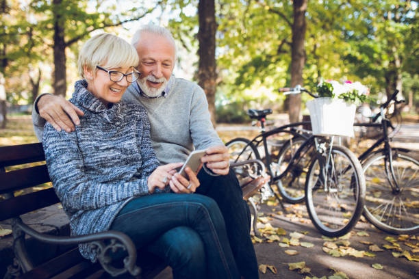 Senior couple using smart phone outdoors Senior couple using smart phone outdoors. park bench photos stock pictures, royalty-free photos & images