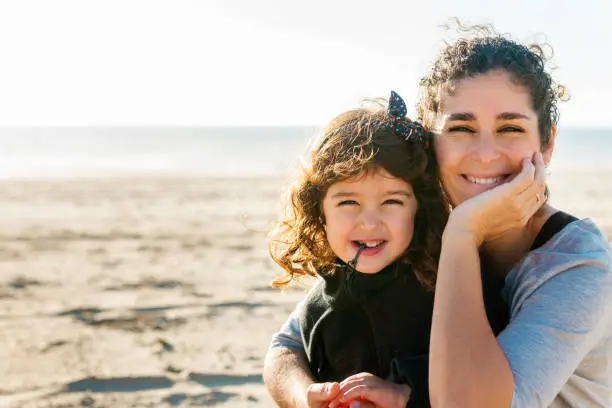 mom and daughter pose smiling and fun on the beach in winter