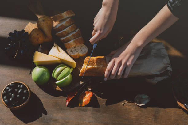 cropped shot of woman slicing baguette on table with fallen leaves