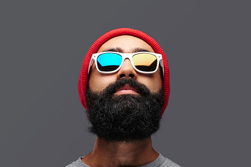Portrait of bearded male with a red cap and colorful glare in sunglasses.