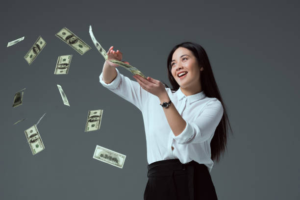 istock smiling asian girl throwing dollar banknotes isolated on grey 916226530