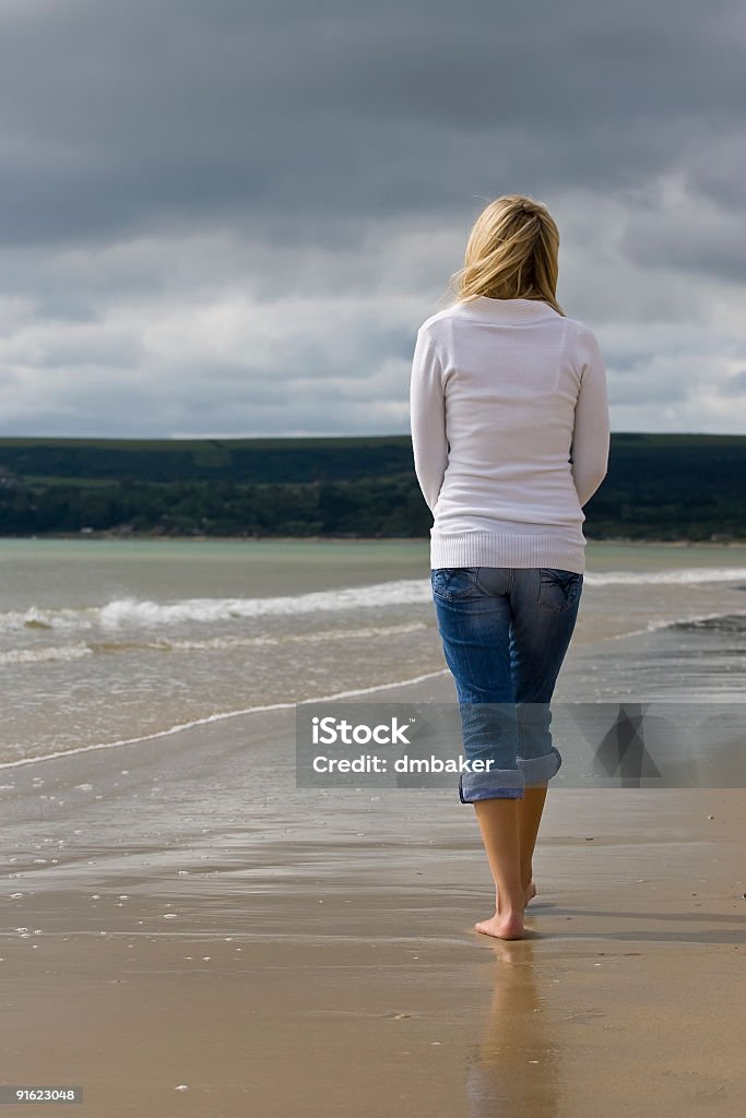 Rear View of Woman On A Beach With Stormy Skies A young woman walks alone on a beach heading towards storm clouds Adult Stock Photo