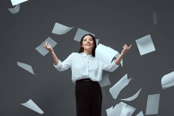 istock smiling young businesswoman throwing papers isolated on grey 916231210