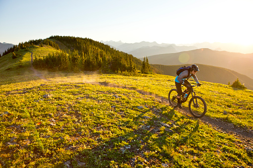 A male teenager rides his mountain bike in the Rocky Mountains of Canada. He is riding an enduro-style mountain bike and wearing a hydration backpack.