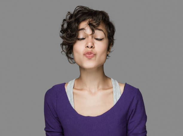 Portrait of young woman blowing a kiss Portrait of young woman blowing a kiss over isoalted gray background. Image taken with Hasselblad H3D camera system and developed from camera RAW puckering stock pictures, royalty-free photos & images