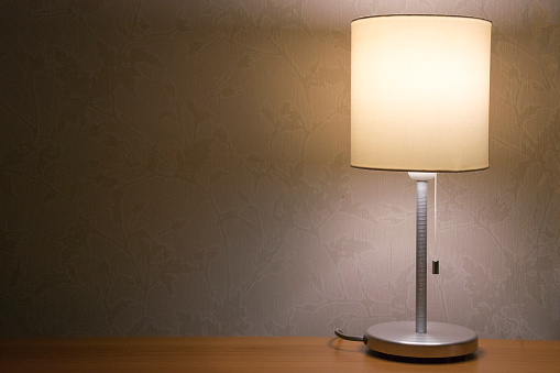 Table lamp over white wall background. Modern minimalistic night light, decorative element for bedroom interior.