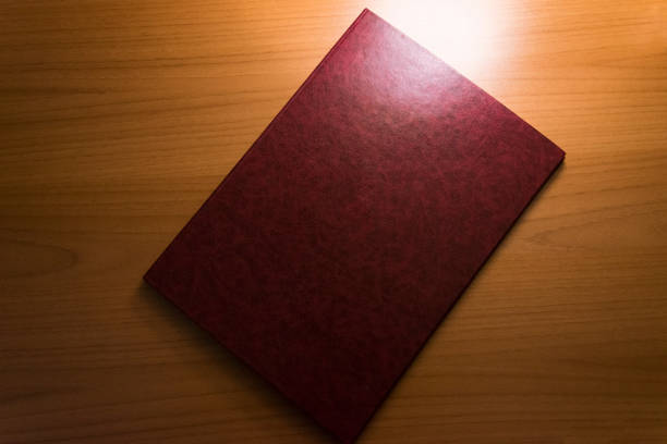 Top view of closed red cover notebook on wooden textured surface. Diary book on desk or table background.