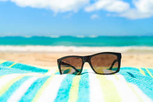 Close up image of sunglasses on the beach towel. Tropical beach, holiday background.