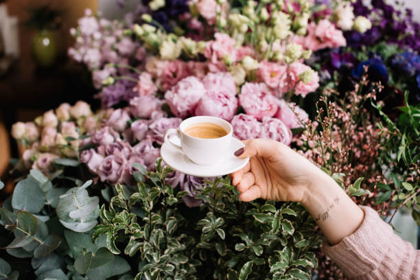 Human's hand holding delicious cup of fresh coffee over blossoming variety of flowers at the florist shop Human's hand holding delicious cup of fresh coffee over blossoming variety of flowers at the florist shop wrist tattoo stock pictures, royalty-free photos & images