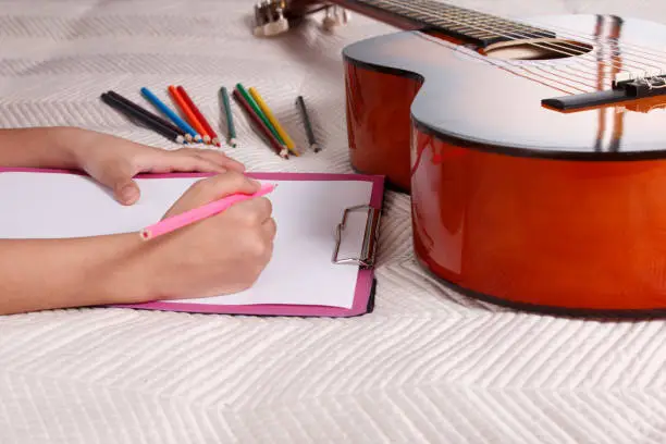The child draws with pencils on paper. Next to it lies the guitar as a symbol of musicality.