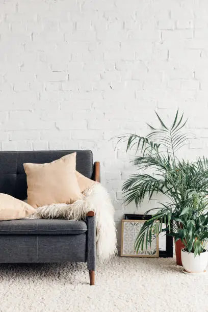 Photo of comfy couch with flowerpots in white living room interior with brick wall, mockup concept