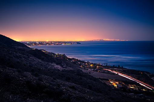 An overlooking view of Pacific Coast Highway curving around the coast line at Leo Carrillo State Beach, California at night, looking toward Malibu and Pointe Dume, with the Santa Monica bay and Palos Verdes peninsula in the far background.