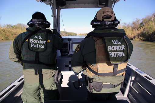 McAllen, Texas, USA - January 29, 2018: Two Border Patrol agents on a small river patrol boat monitor the Rio Grande River for illegal aliens crossing into the U.S. Such encounters are a daily experience in the Rio Grande Valley sector of Border Patrol operations.