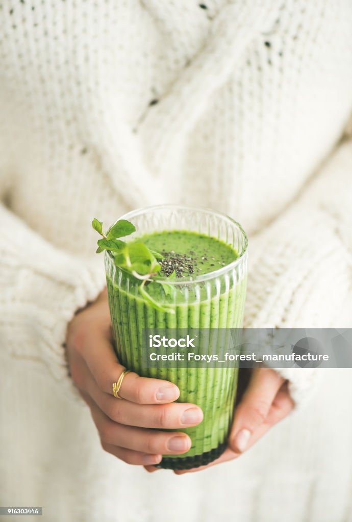 Matcha green vegan smoothie with chia seeds and mint Matcha green vegan smoothie with chia seeds and mint in glass in hands of female wearing white sweater. Clean eating, detox, alkaline diet, weight loss concept Smoothie Stock Photo