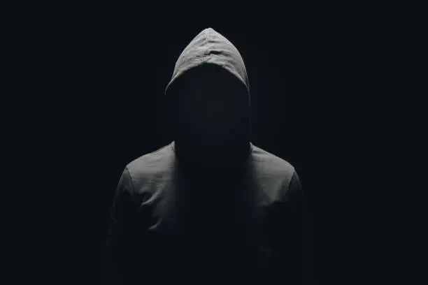 Photo of faceless man in hoodie standing isolated on black