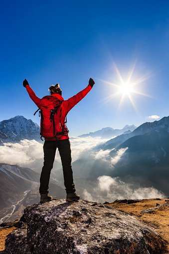 Young woman, wearing red jacket, lifts her arms in victory. She is standing on the top of a mountain and watching sunset over Himalayas .Mount Everest National Park. This is the highest national park in the world, with the entire park located above 3,000 m ( 9,700 ft). This park includes three peaks higher than 8,000 m, including Mt Everest. Therefore, most of the park area is very rugged and steep, with its terrain cut by deep rivers and glaciers. Unlike other parks in the plain areas, this park can be divided into four climate zones because of the rising altitude.