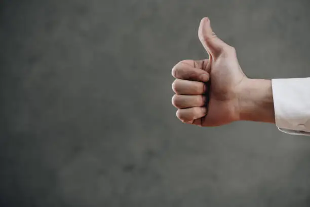 Photo of cropped shot of man showing thumb up on grey