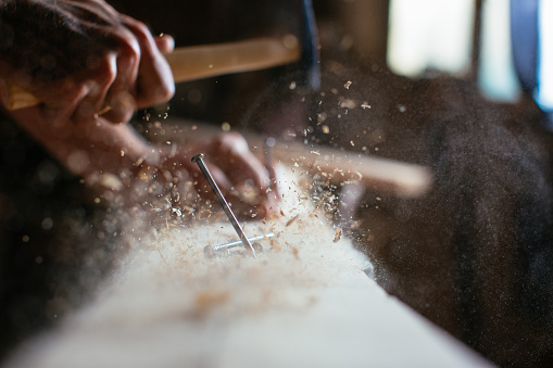 Close up of man hammering a nail into wooden board. Shallow DOF. Developed from RAW; retouched with special care and attention; Small amount of grain added for best final impression. 16 bit Adobe RGB color profile.