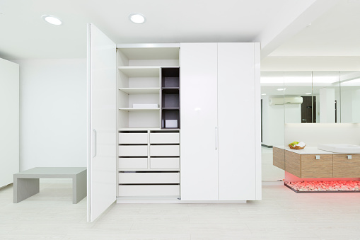 Empty dressing room with white laminate wood cabinet, an open door show shelves, drawers and other storage compartments. Wood laminate flooring. Bathroom on the side Modern design. Residential Room Horizontal orientation photography.