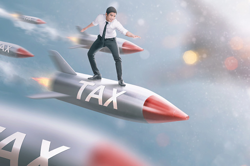 Handsome asian businessman flying on tax rocket. Taxation concept