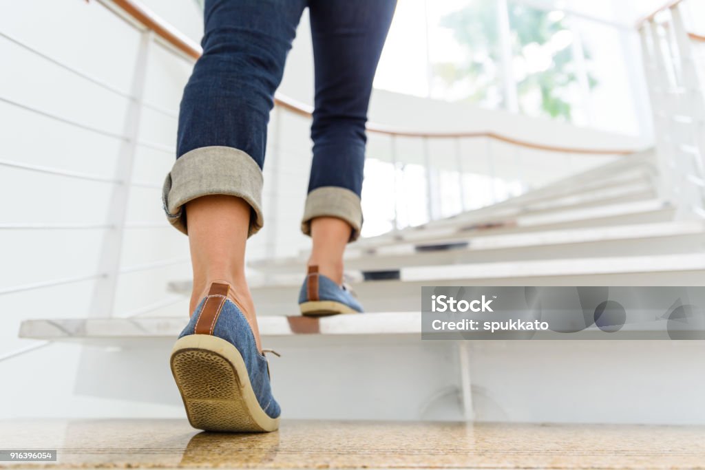 Young adult woman walking up the stairs with sun sport background. Staircase Stock Photo