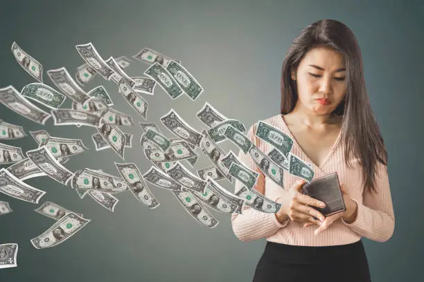 Photo of poor Asian woman holding  purse having problem with money flying away, over spending concept