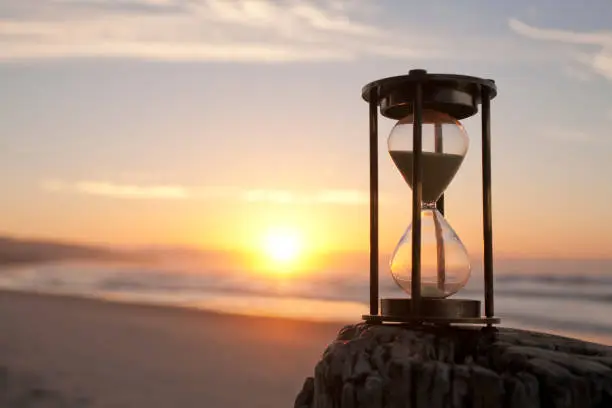 An hourglass on a beach in front of a beautiful sunrise, shallow DOF.