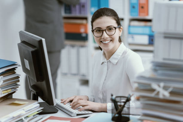 joven secretaria trabajando y sonriendo - empleado de archivo fotografías e imágenes de stock