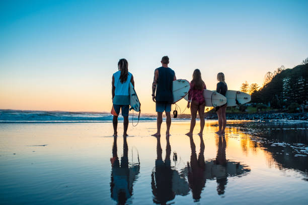 istock Group of friends standing at the sandy beach with surfboards 916438006