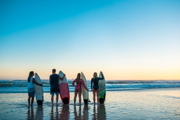 istock Four friends standing at the beach with surfboards 916438008