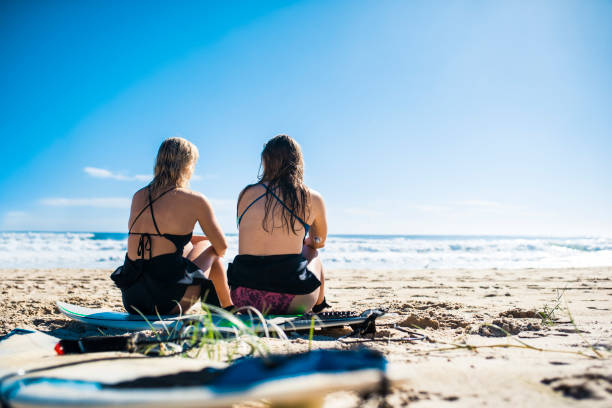 istock Two friends sitting on a surfboard at the beach 916438178