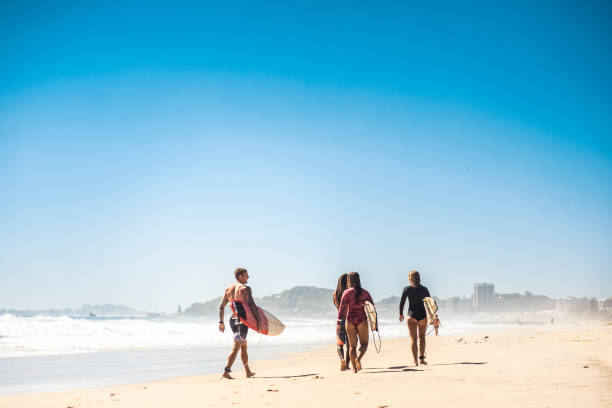istock Small group of people walking on the beach with their surfboards 916438252