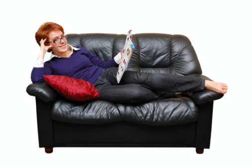 Red-haired girl is laying on sofa and reading magazine