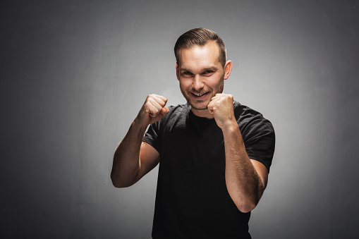Man showing his fists and smiling cheeky to the camera. Demonstration of power. Studio portrait.