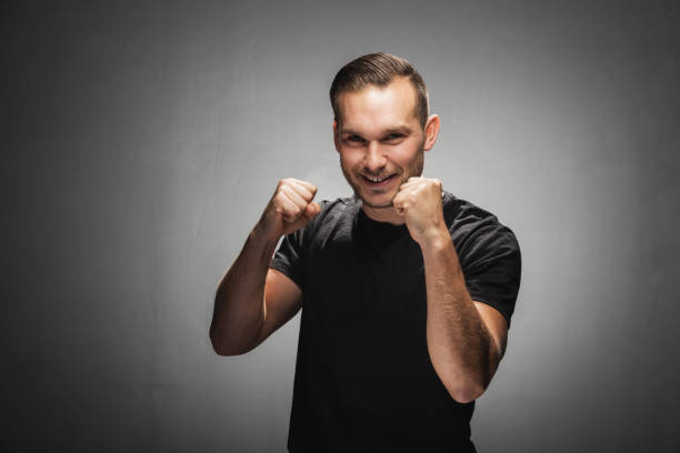 Happy man in a fighting position. Man showing his fists and smiling cheeky to the camera. Demonstration of power. Studio portrait. fighting stance stock pictures, royalty-free photos & images