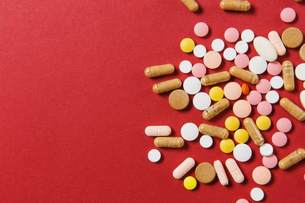 istock Medication white colorful round tablets arranged abstract on red color background. Aspirin, capsule pills for design. Health, treatment, choice healthy lifestyle concept. Copy space advertisement. 916449690