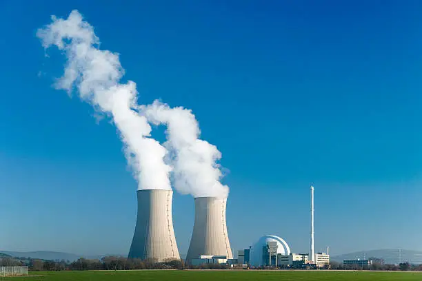 Nuclear power station with two steaming cooling towers in blue sky. 