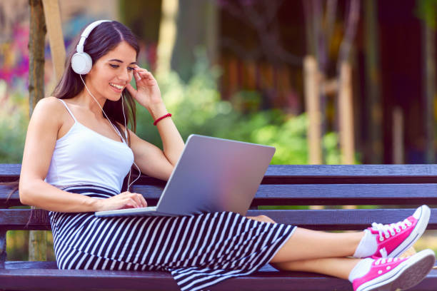 istock Young pretty woman sitting on bench in the park, using laptop computer 916460620