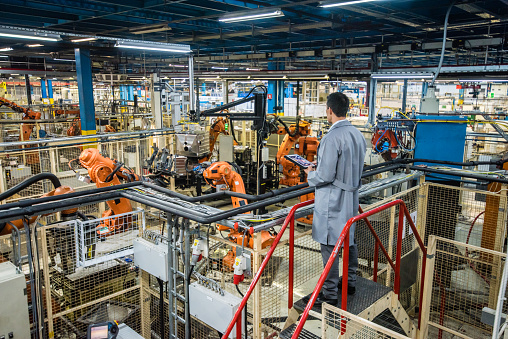 Male factory engineer inspecting the work process of the robots performing their operations in appliance manufacturing factory.