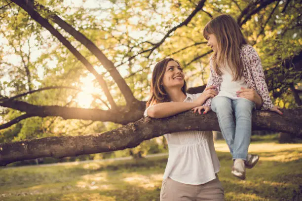 Photo of Cute little girl sitting on tree branch and looking at mother