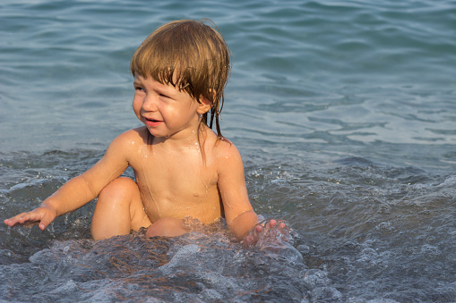 Portrait smiling little baby playing in the sea ocean. Positive human emotions feelings joy. Funny cute child making vacations and enjoying summer.